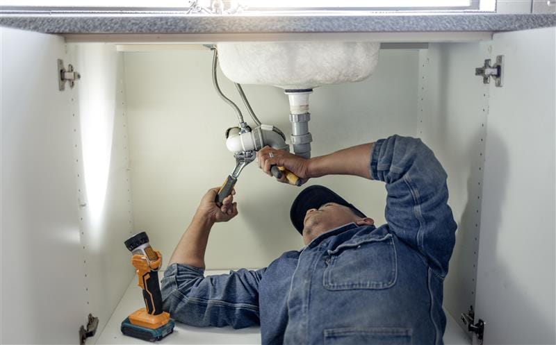 Plumber repairing pipes beneath a bathroom sink in Coral Springs