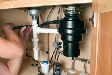 Plumber repairing a garbage disposal beneath a kitchen sink in Coral Springs