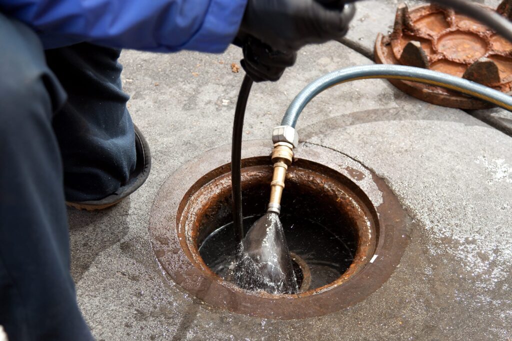 Plumber hydro jetting a sewer line through a manhole in Coral Springs