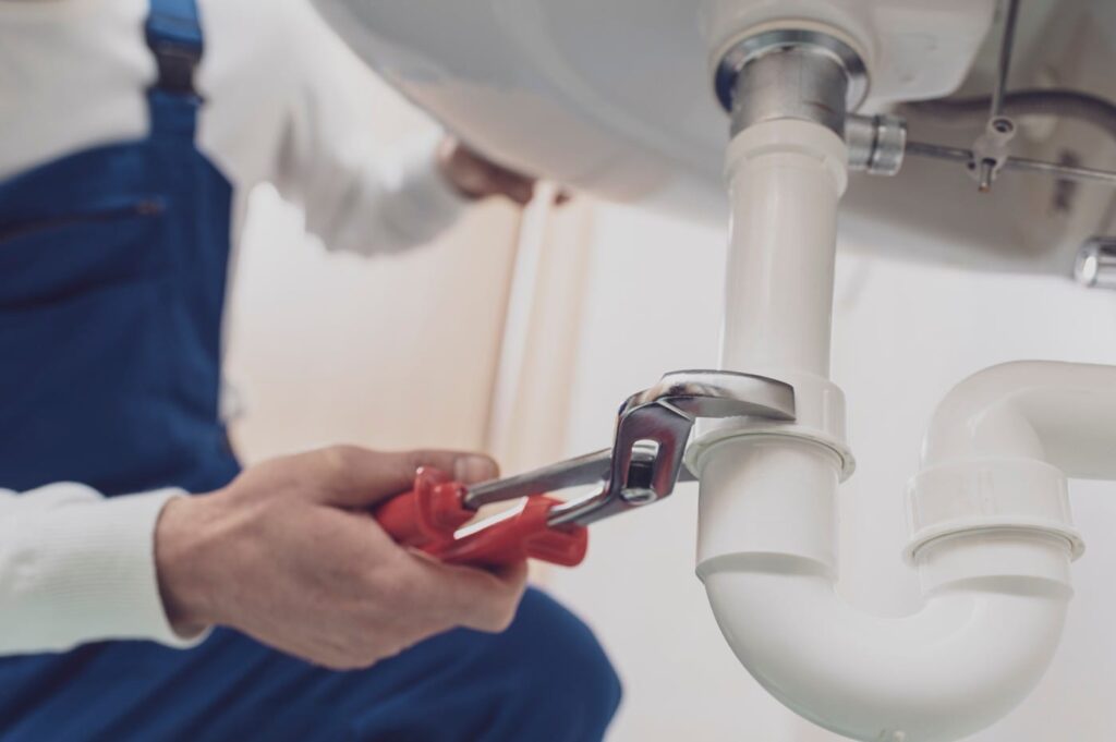 Plumber repairing a white drain pipe beneath a sink in Coral Springs