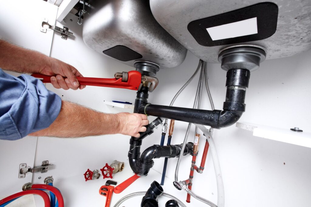 Plumber repairing drain pipes beneath a kitchen sink in Coral Springs